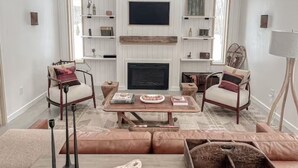 A modern living room with a fireplace, two armchairs, a coffee table, and a TV mounted on the wall. - The Cork Cottages, Unit 1, Arcade Table, Modern and New 2b/2b (Geneva)