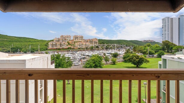 A view from a balcony overlooking a marina with boats, a green landscape, and a large building with multiple balconies. - Marina Avenue by Otium (Fajardo)