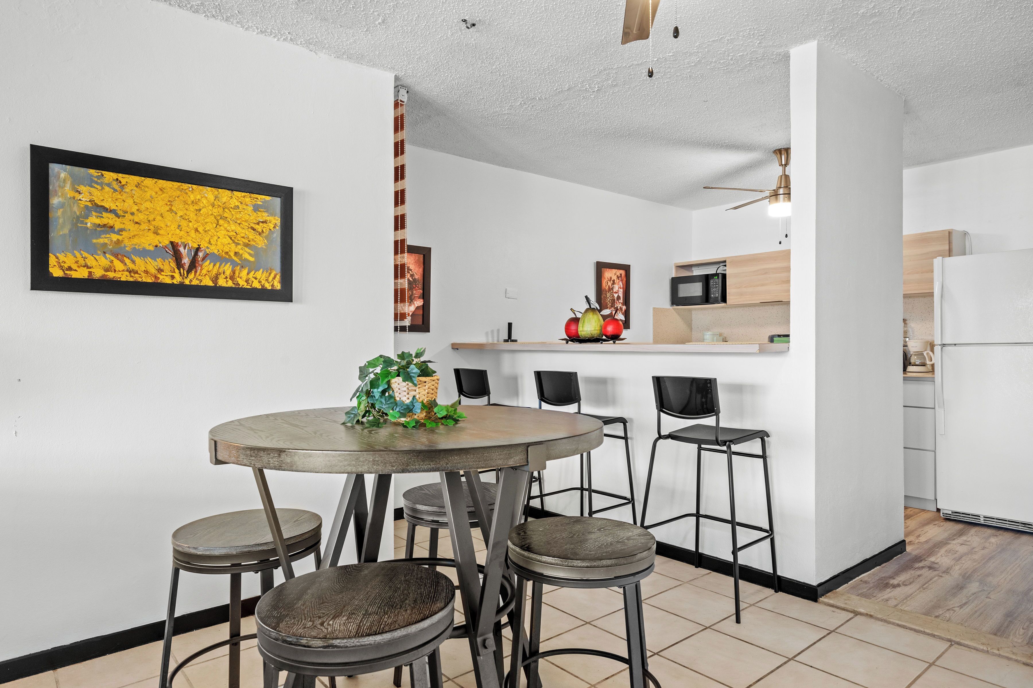 A modern kitchen with white cabinets, a microwave, and a refrigerator. There is a dining area with a round table and four stools.