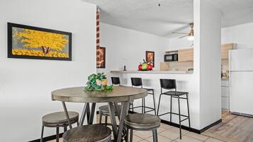 A modern kitchen with white cabinets, a microwave, and a refrigerator. There is a dining area with a round table and four stools.