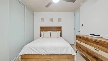 A bedroom with a bed, a wooden dresser, a ceiling fan, and a light fixture.