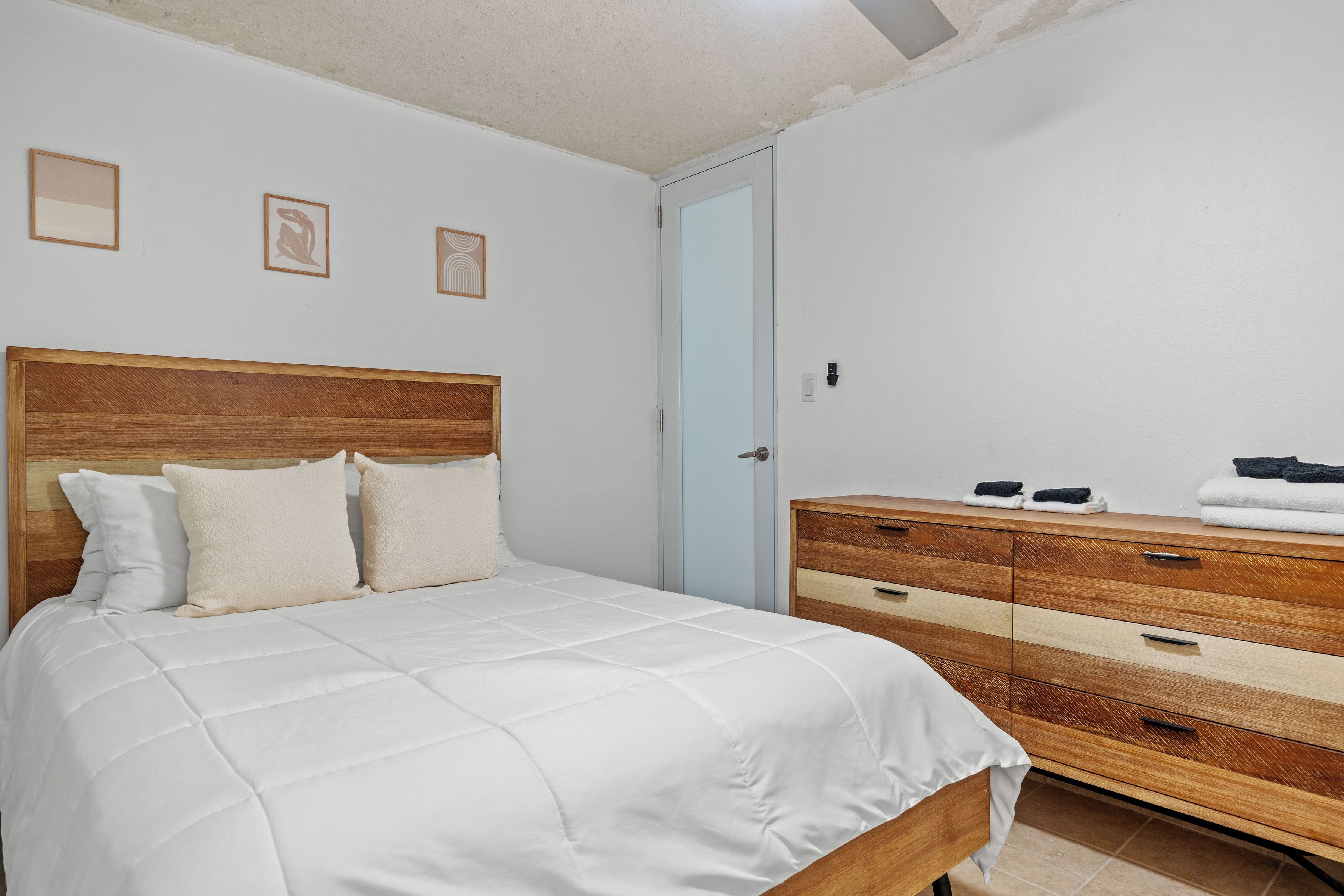 A bedroom with a wooden headboard bed, a wooden dresser with drawers, and a light blue door.