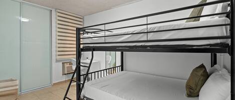 Un lit superposé avec une échelle, un matelas blanc et des oreillers. Il y a une petite table et une chaise dans le coin.