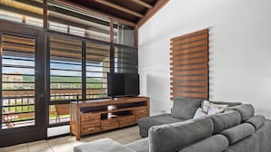 A living room with a grey sofa, a wooden TV stand, and a large window with blinds. - Marina Avenue by Otium (Fajardo)