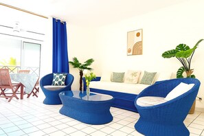 Ein Wohnzimmer mit einer Couch, zwei blauen Sesseln, einem Couchtisch und einem Essbereich mit Tisch und Stühlen.