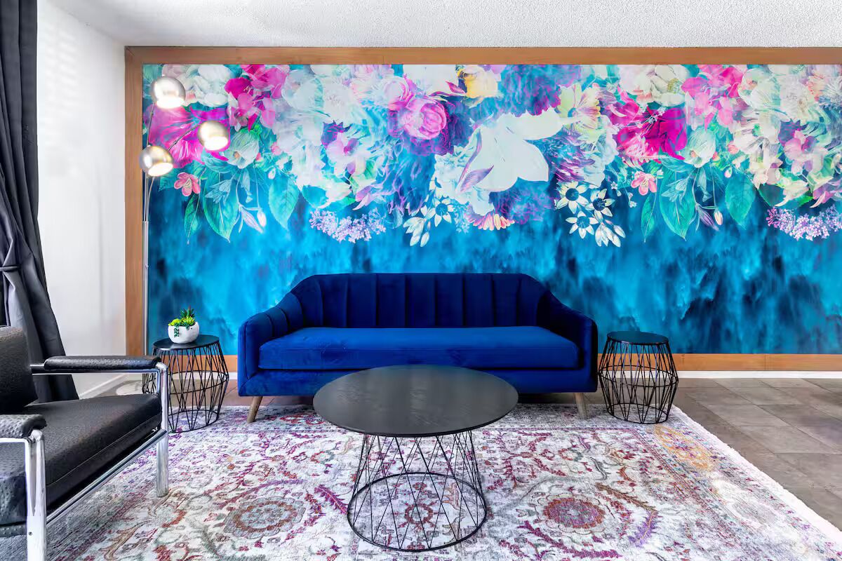 A room with a blue sofa, a round black table, and a floral mural on the wall.