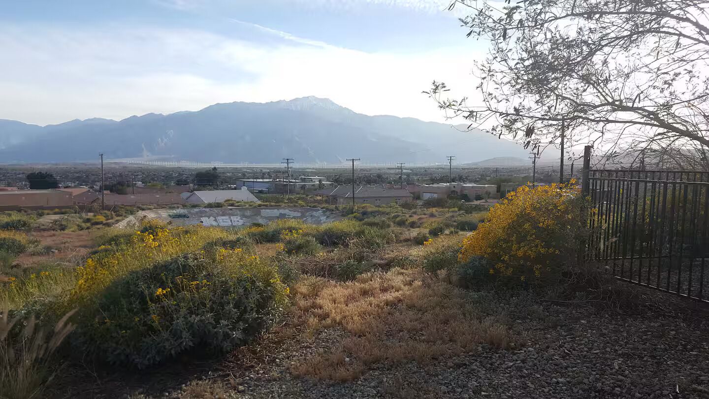 A rural landscape with mountains in the background, a fenced area with sparse vegetation, and utility poles.