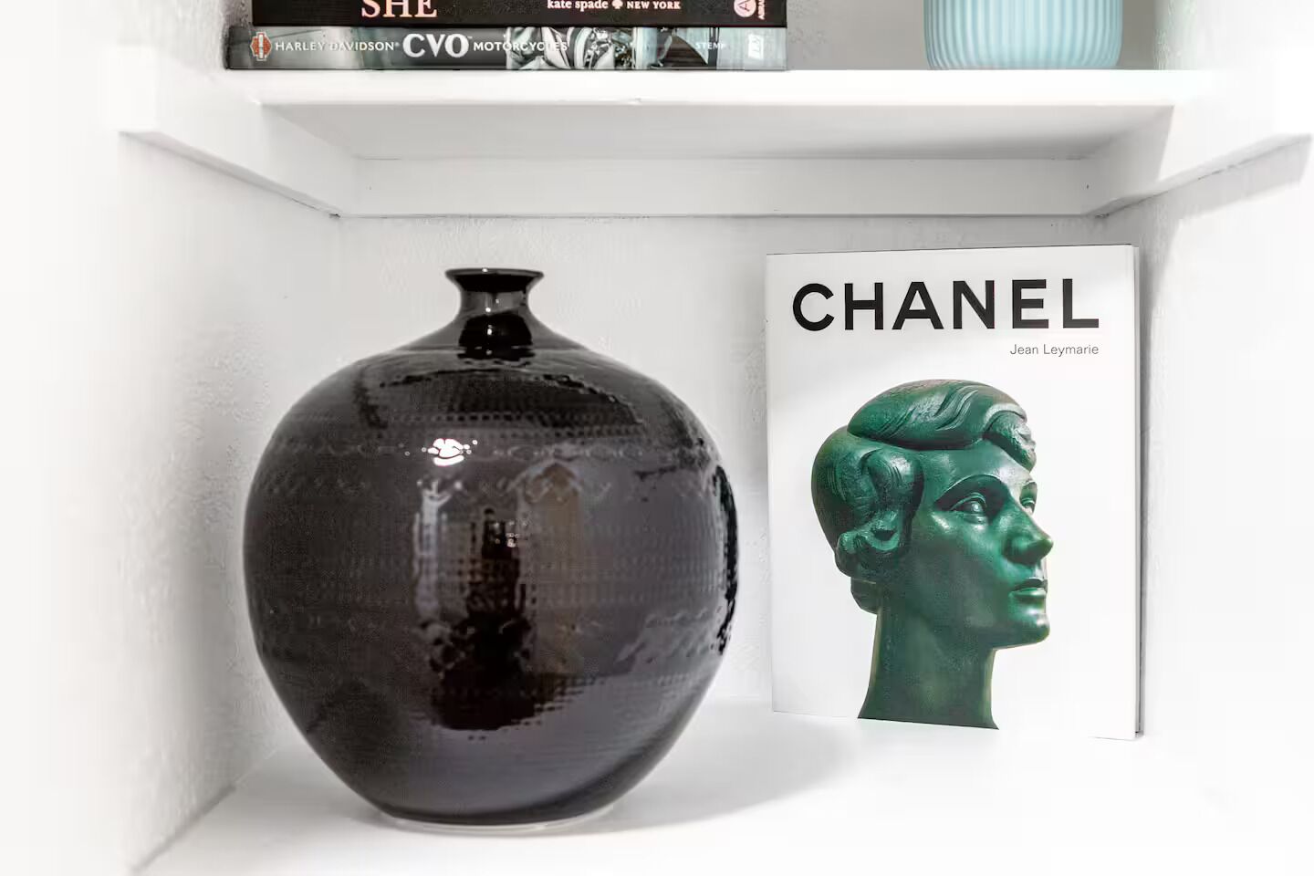 Un jarrón negro sobre una estantería con un libro titulado 'CHANEL' a su lado.