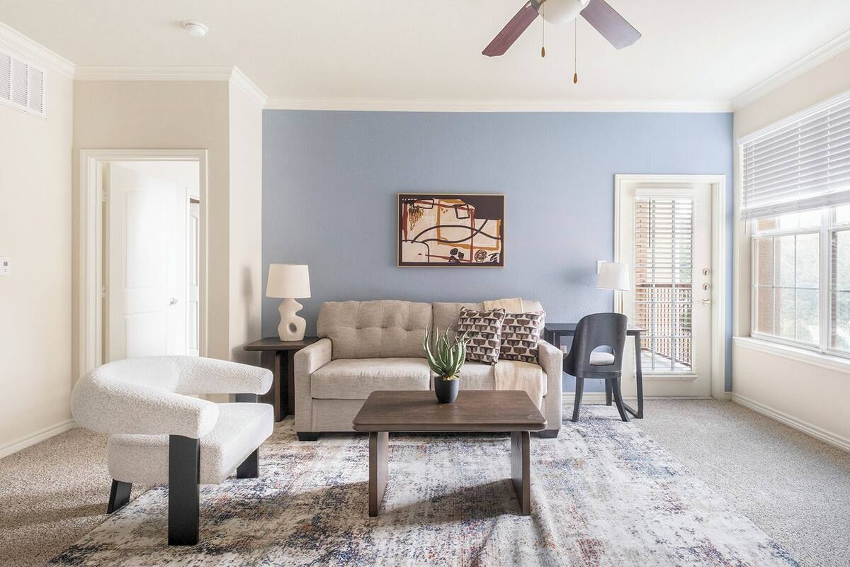 A living room with a beige sofa, a coffee table, a white armchair, and a blue accent wall.