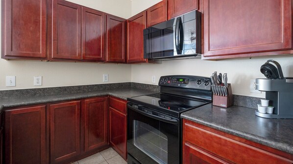 A kitchen with dark wooden cabinets, a black microwave, a stove, and a coffee maker. - Landing Furnished Apartments Northwest Houston (Houston)