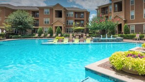 Ein Swimmingpool mit Liegestühlen und einer Fontäne, umgeben von Mehrfamilienhäusern.