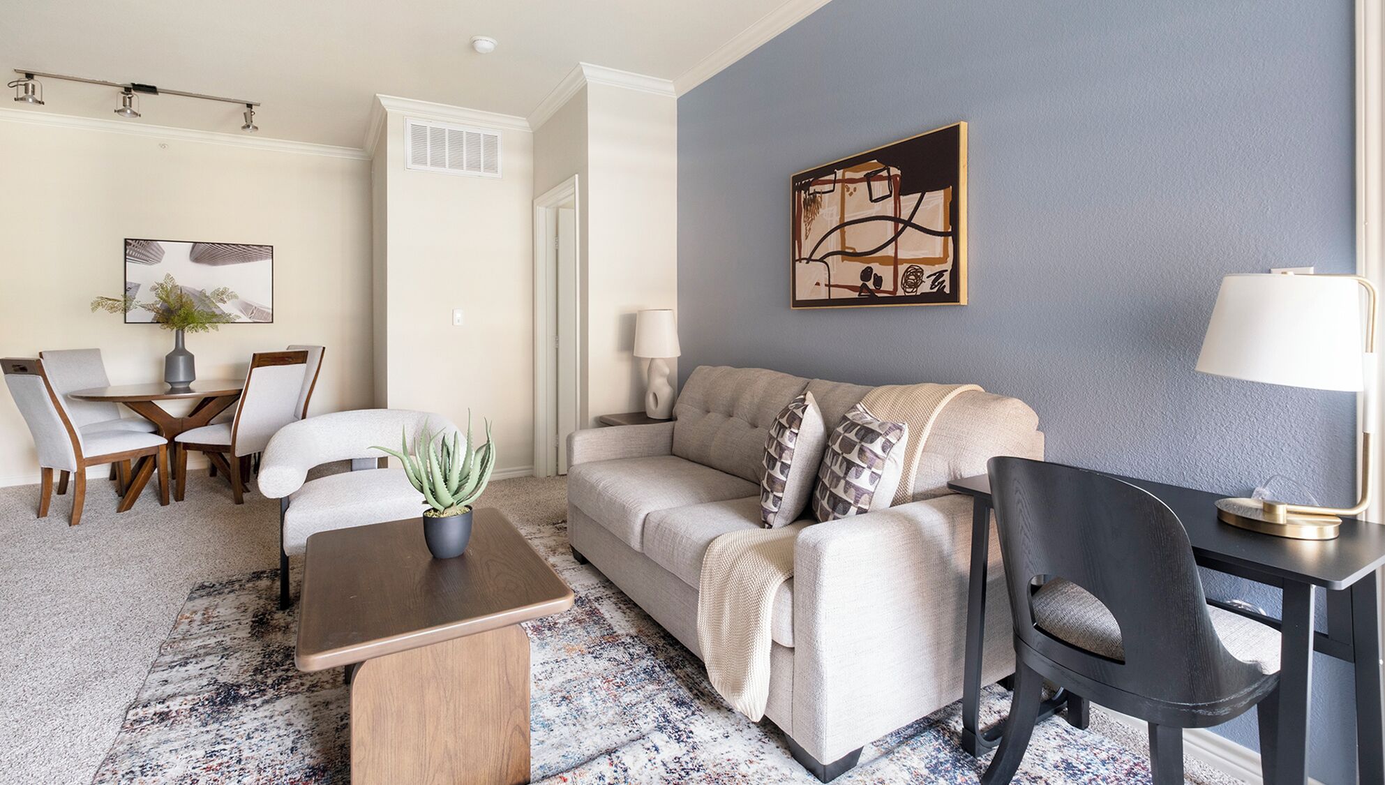 A living room with a sofa, a coffee table, a dining table with chairs, a lamp, and a painting on the wall.