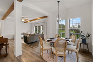 Un vaste espace dédié à la salle à manger, avec une table en bois, des chaises en osier et un lustre.