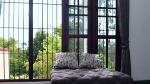 A bedroom with a large window, a bed with a tufted headboard, and two floral pillows. - Thimira Mist - Mountain-View Home (Kandy)