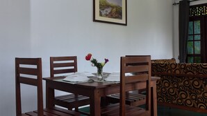 A dining area with a round table, four wooden chairs, a vase with flowers, and a framed picture on the wall. - Thimira Mist - Mountain-View Home (Kandy)
