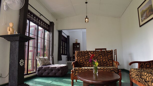 A room with a patterned sofa, a round wooden table with a vase, a decorative pillar, and a fan. - Thimira Mist - Mountain-View Home (Kandy)