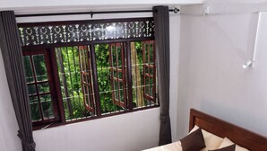 A bedroom with a bed, pillows, a wooden headboard, a window with a view of greenery, and a red carpet. - Thimira Mist - Mountain-View Home (Kandy)