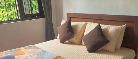 Una cama bien hecha con colcha, almohadas y una toalla enrollada.