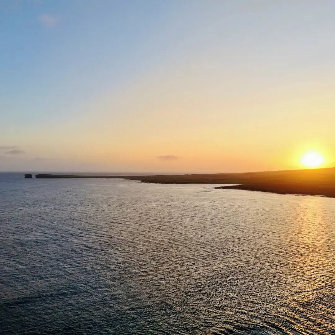 A coastal sunset view with calm waters and a distant landmass.