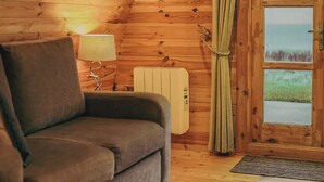 A cozy room with a wooden ceiling, a sofa, a lamp, a radiator, and a door with a view. - Ceide Glamping  (Ballycastle)