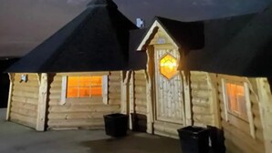 A wooden cabin with a sloped roof, a chimney, and a lit entrance. - Ceide Glamping  (Ballycastle)