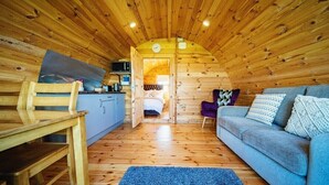 A cozy cabin interior with a wooden ceiling, a sofa, a chair, a small table, and a bed. - Ceide Glamping  (Ballycastle)