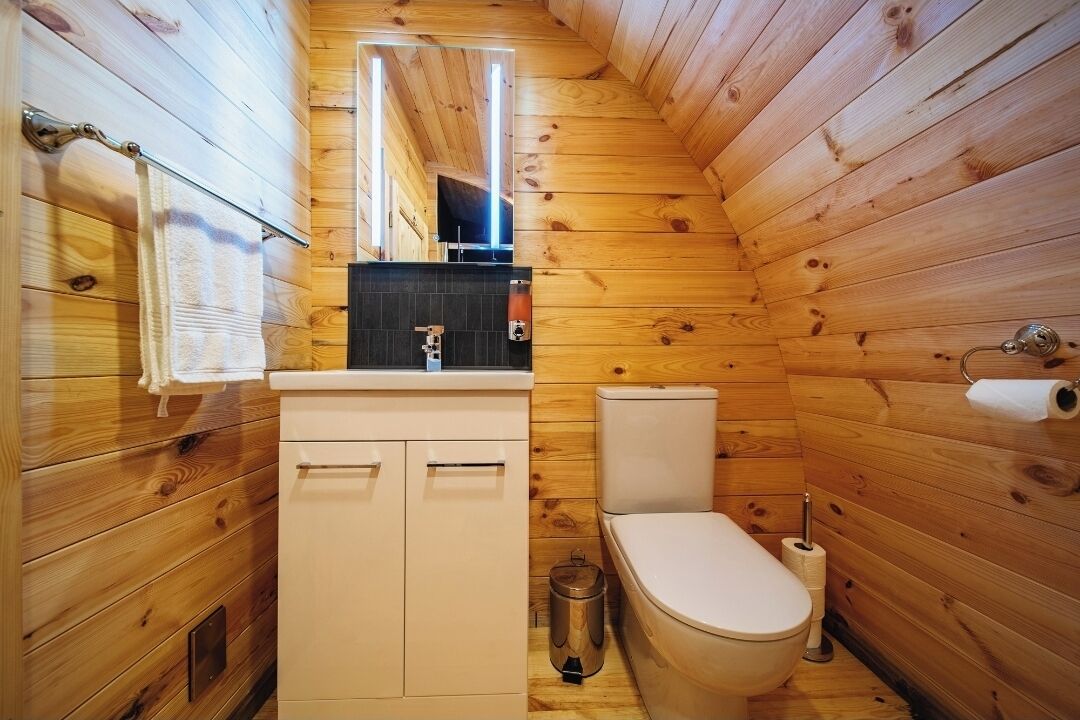 Ein kleines Badezimmer in einer Holzblockhütte mit Toilette, Waschbecken und Spiegel.