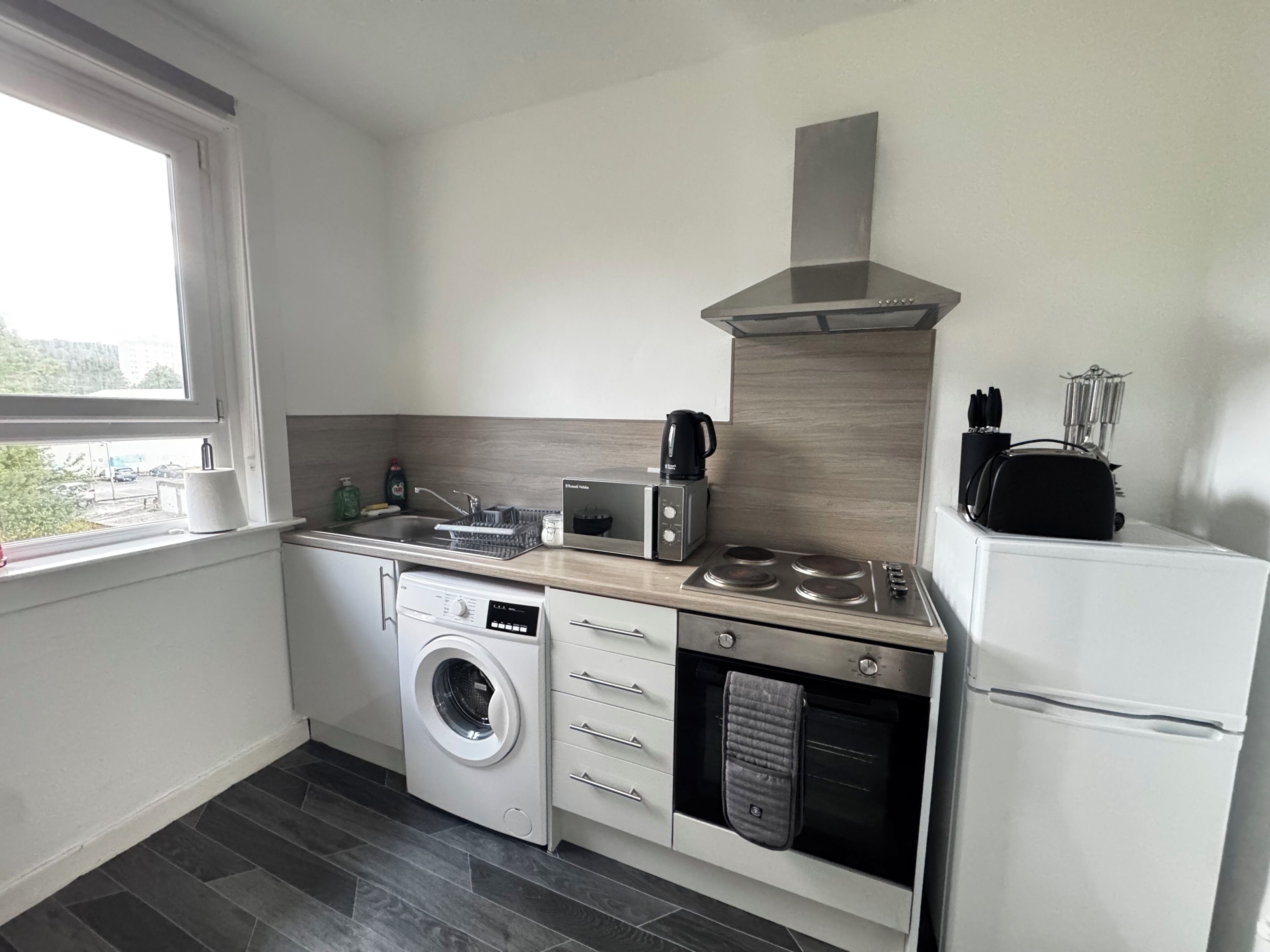 A compact kitchen with a washing machine, a coffee maker, and a built-in oven.