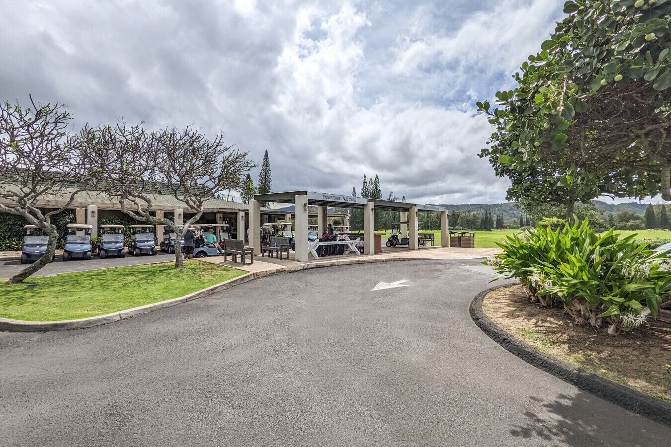 A golf course entrance with a covered pavilion, a parking area, and a well-maintained lawn.