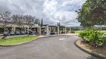 A golf course entrance with a covered pavilion, a parking area, and a well-maintained lawn.