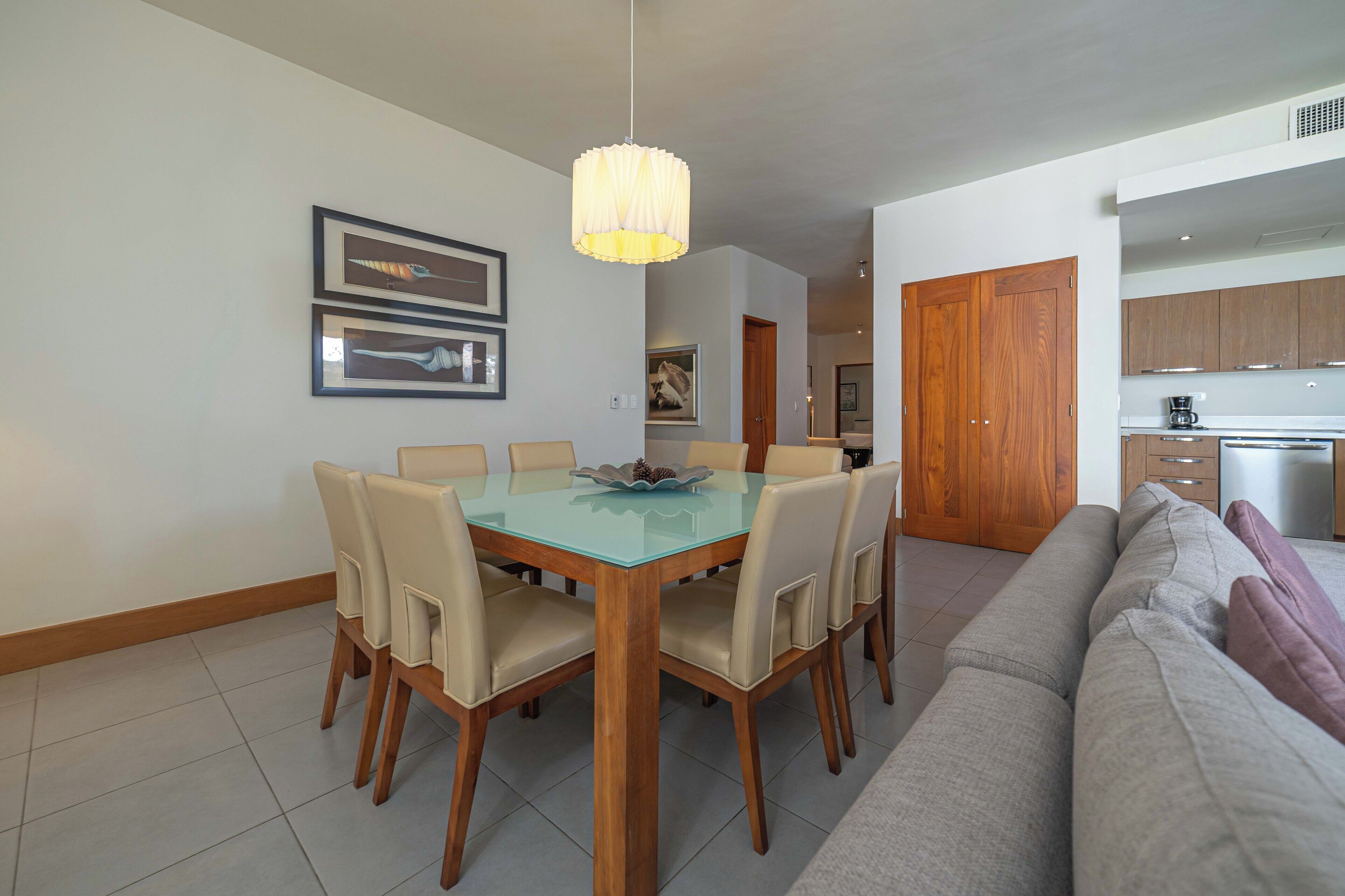 A dining area with a glass table, wooden chairs, and a pendant light.