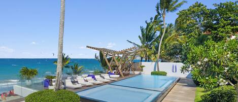 Un espace piscine avec des chaises longues, une pergola en bois et une vue sur l’océan.