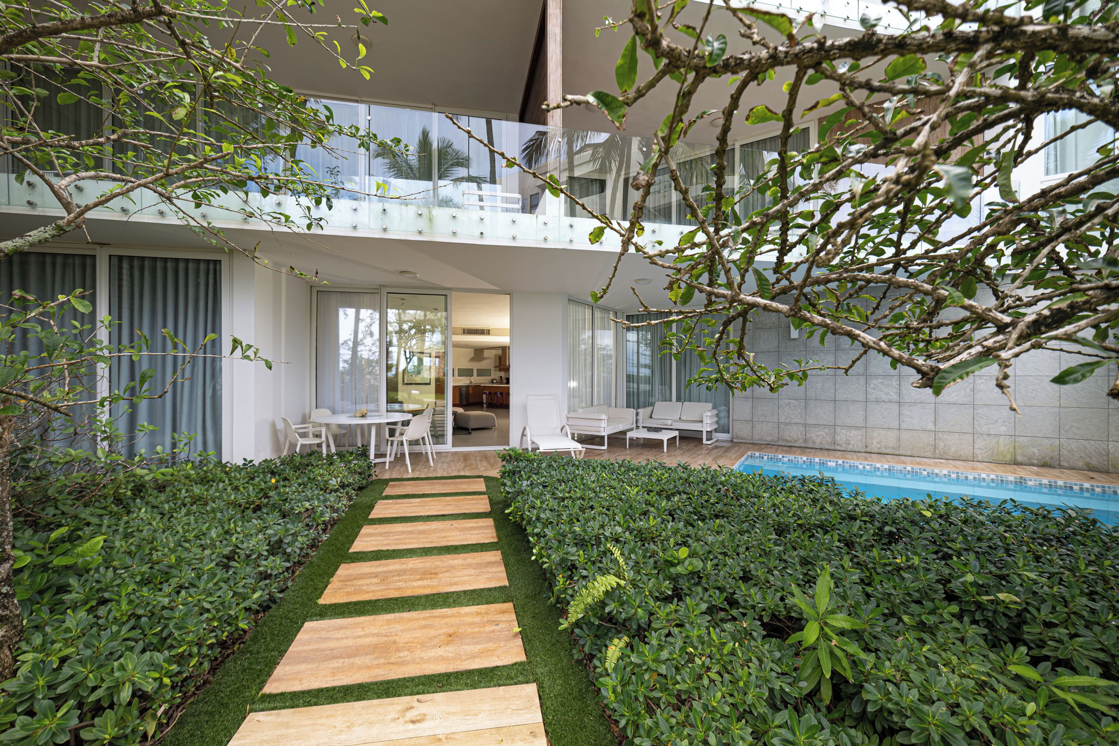 A modern building with a glass balcony, a pool, and a wooden pathway.