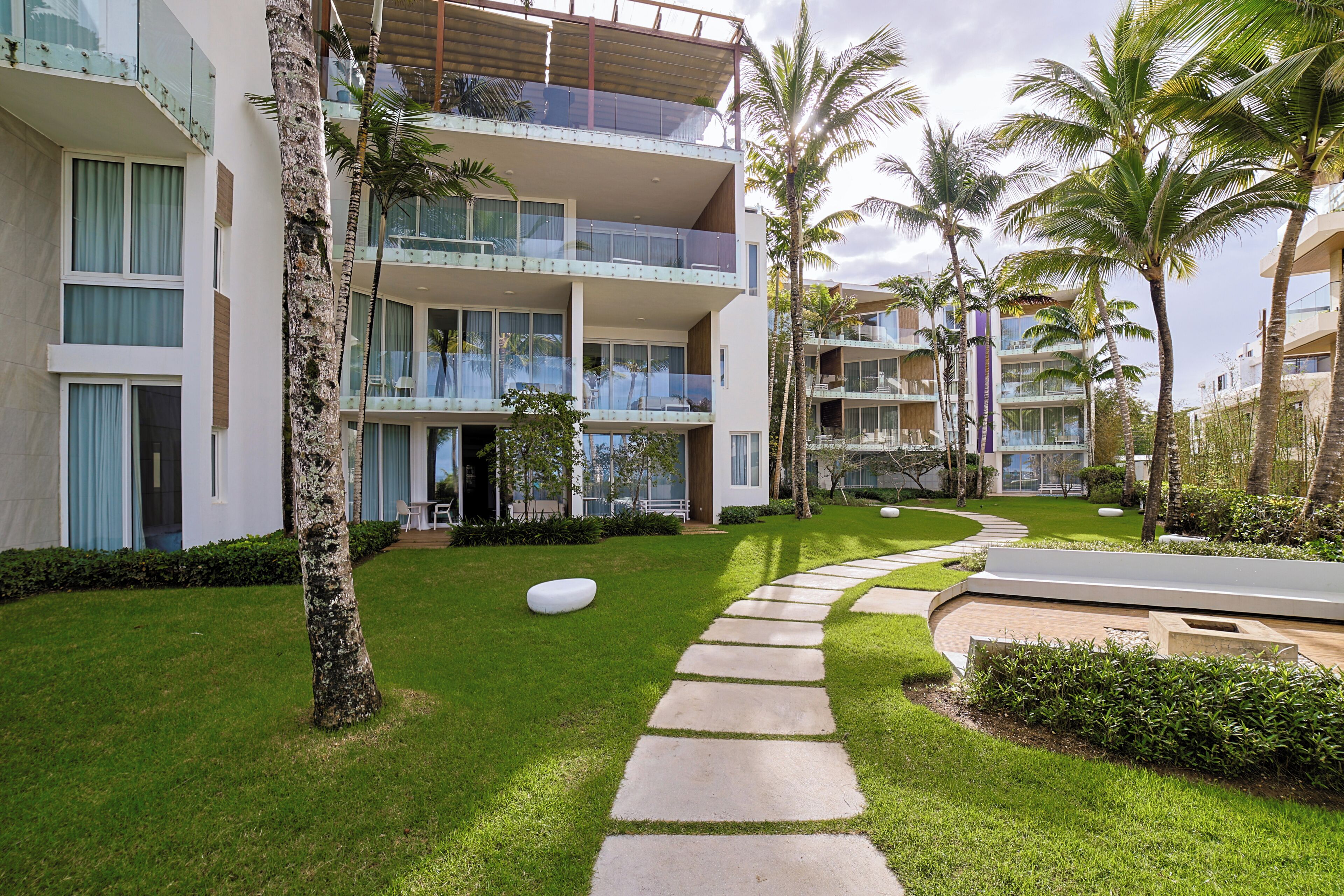 Un hôtel moderne à l’architecture contemporaine, avec deux étages, des balcons et une pelouse bien entretenue agrémentée de palmiers.