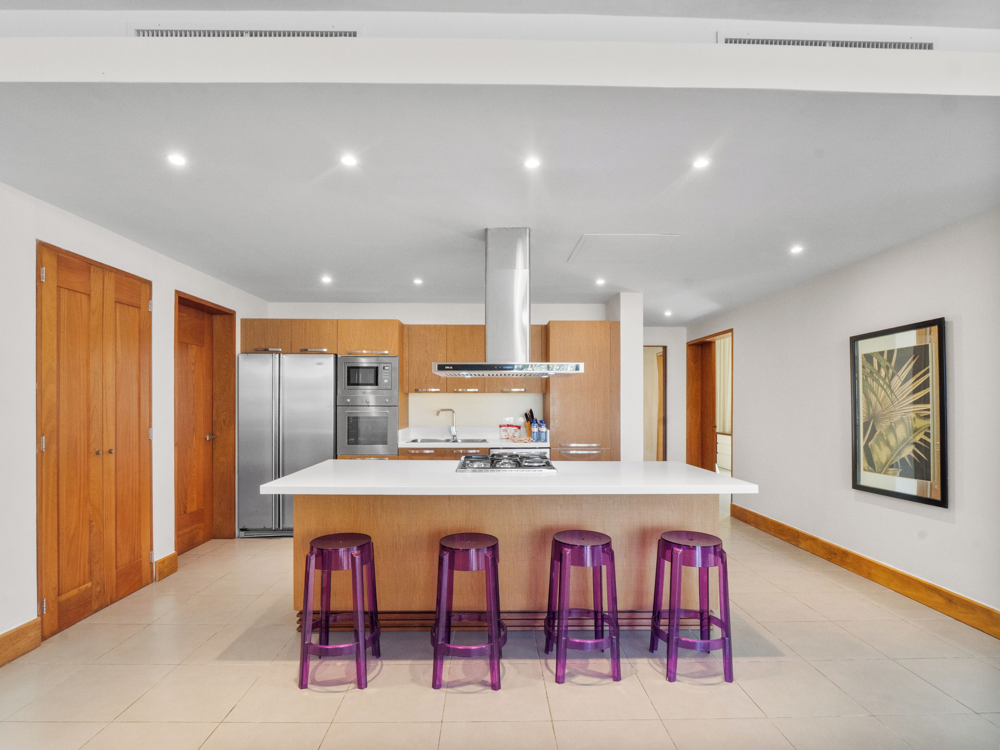 A modern kitchen with a central island, stainless steel appliances, wooden cabinets, and a large window.