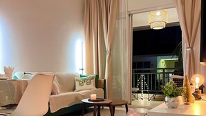 Un salon chaleureux avec un canapé, des fauteuils, une petite table sur laquelle est posée une bougie, et un fauteuil en osier.