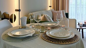 Une table à manger dressée avec des assiettes, des verres et des couverts, avec un canapé et des rideaux en arrière-plan.
