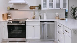 A modern kitchen with white cabinetry, stainless steel appliances, and a built-in dishwasher. - The Cottage (Brevard County)