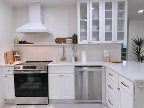 A modern kitchen with white cabinetry, stainless steel appliances, and a built-in dishwasher. - The Cottage (Brevard County)