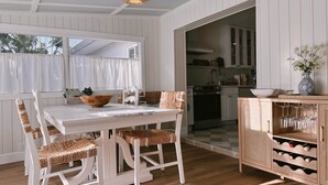 A dining area with a white table and chairs, a woven ceiling light, and a kitchen visible through an open doorway. - The Cottage (Brevard County)