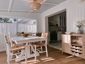 A dining area with a white table and chairs, a woven ceiling light, and a kitchen visible through an open doorway. - The Cottage (Brevard County)
