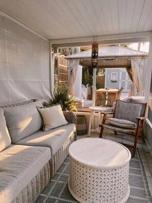 A covered outdoor seating area with a sofa, chair, table, and decorative umbrella. - The Cottage (Brevard County)