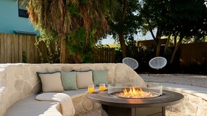 A stone outdoor seating area with a fire pit, two chairs, and a table with drinks. - The Cottage (Brevard County)