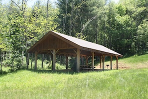 A wooden pavilion with a sloped roof, surrounded by a grassy area and dense forest. - Wintergreens R331- Mtn Condo/View, Gated Resort, Indoor/Outdoor Pools & Hot Tub (Boone)