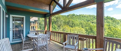 A wooden deck with a table and chairs, overlooking a forested area.