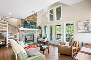 Amplia sala de estar con chimenea, una escalera y un balcón con vistas a zonas verdes.