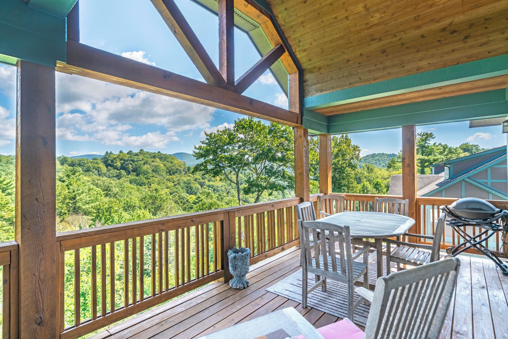 A wooden deck with a table and chairs, overlooking a forested landscape.