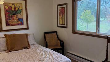 A bedroom with a bed, a chair, a ceiling fan, and two framed pictures on the wall.