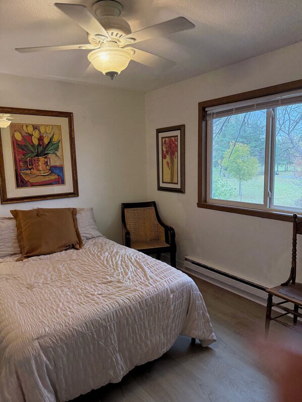 Une chambre à coucher comprenant un lit, une chaise, un ventilateur de plafond et deux tableaux encadrés accrochés au mur.