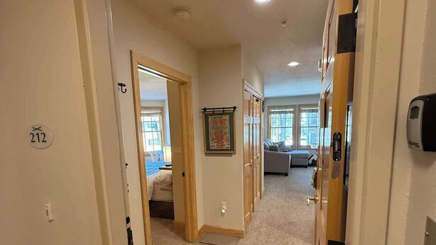 A hallway with carpeted floors, wooden doors, and a bench. There is a door with the number 212 visible.